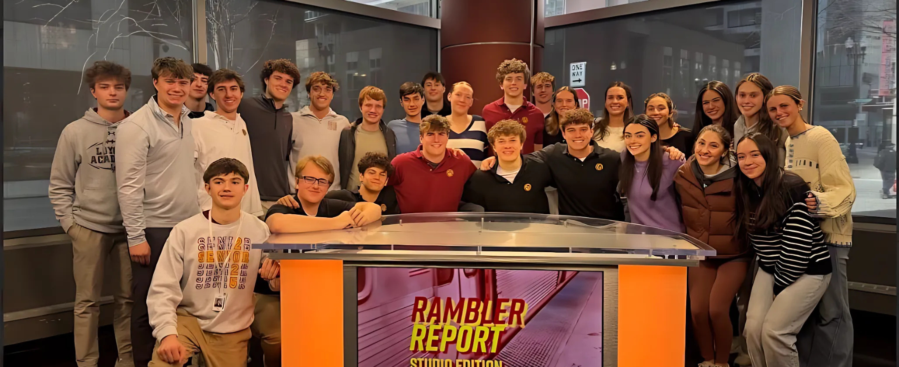 A group photo of students from Loyola Academy gather around the news desk inside of the School of Communication at Loyola Chicago